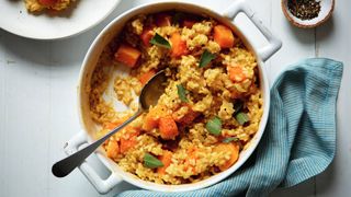 Pot of low-fat butternut squash risotto with a spoon inside and a cloth at the bottom.