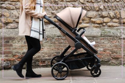 A young woman with long hair and stylish clothes pushes the iCandy Peach 7 pushchair along an urban street